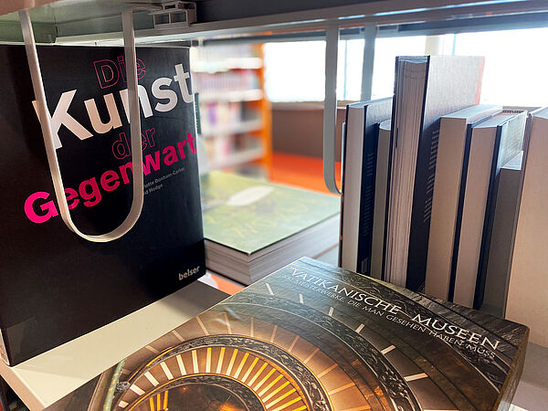 Blick durch ein Bücherregel in der Landesbibliothek. Im Fokus stehen die Titel „Die Kunst der Gegenwart“ und „Vatikanische Museen“. 