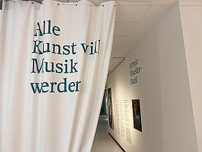 Ein weißer Vorhang am Eingang der Ausstellung. Darauf steht: "Alle Kunst will Musik werden."