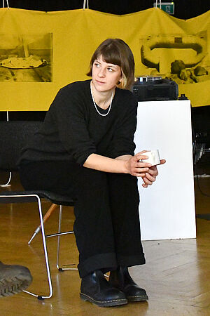 Laura Schöning sitzt auf einem Stuhl vor einer gelben Leinwand.