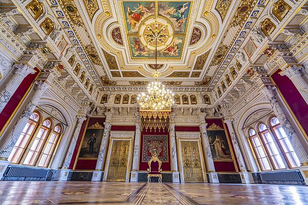 Blick in den Thronsaal des Schweriner Schlosses. Zu sehen sind zwei Fenster rechts und links, ein Kronleuchter oben und der Thron in der Mitte.