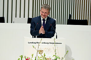 Ein Mann steht an einem Pult und spricht ins Mikrofon.