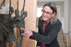 Eine Frau zeigt mit dem Finger auf eine Metallskulptur.