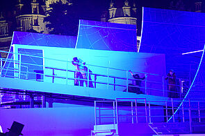 Das Deck im Bühnenbild neigt sich. Frauen und Männer halten sich am Geländer fest. 