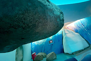 Ein großer Findling ragt von links ins Bild. im Hintergrund steht ein echter Eisberg. Daneben liegen weitere Findlinge. 