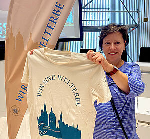 Eine Frau hält ein weißes Shirt hoch. Auf dem Shirt steht "Wir sind Welterbe". Darunter befindet sich eine Silhouette von Schwerin.