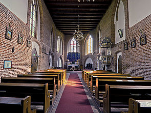 Eine Kirche von innen. Links und rechts stehen Holzbankreihen. Am Ende des Raums befindet sich der Altar.