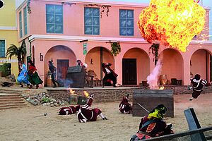 Ein Bühnenbild mit einem spanischen Haus im Hintergrund. Davor eine Feuerfontäne und laufende Menschen.
