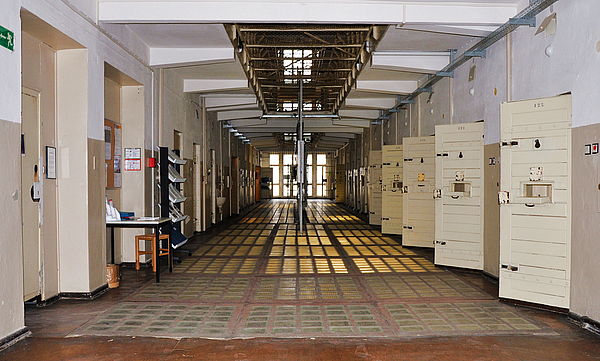 Ein Zellentrakt der Stasi-U-Haft Rostock. Rechts reiht sich Zellentür an Zellentür. Die Türen sind geöffnet.