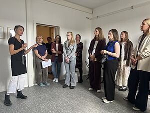 Mehrere Menschen stehen in einem Raum. Links steht eine Frau und spricht.