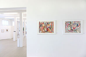 Farbige Bilder hängen im weißen Ausstellungsraum.