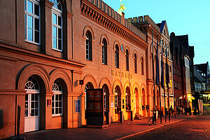 Abenddämmerung am Schweriner Markt. Im Fokus: Das alte Rathaus. Die Beleuchtung des Markts lässt das Orange der Rathausfassade sanft in der Dämmerung schimmern.