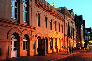 Abenddämmerung am Schweriner Markt. Im Fokus: Das alte Rathaus. Die Beleuchtung des Markts lässt das Orange der Rathausfassade sanft in der Dämmerung schimmern. 