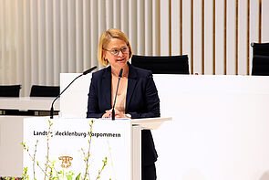 Eine Frau steht an einem Pult und spricht ins Mikrofon.