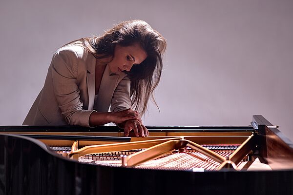 Die ukrainische Pianistin Kateryna Titova sitzt vertieft am Flügel. Sie trägt einen hellen Blazer und schaut konzentriert auf die Tasten des geöffneten Klaviers. Die Szene ist in sanftem Licht gehalten, was die kontemplative Stimmung des Bildes unterstreicht.