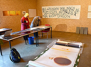 Rico steht mit einem Mitglied der Kunstkommission in ihrem Atelier und zeigt ihre Arbeiten.