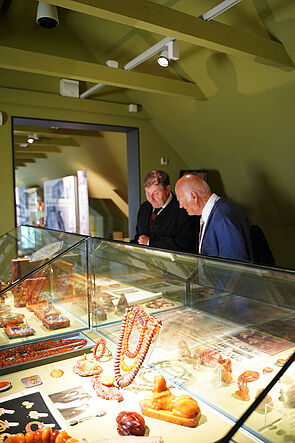 Besucher schauen in eine Vitrine. In der Vitrine liegt Schmuck aus Bernstein.