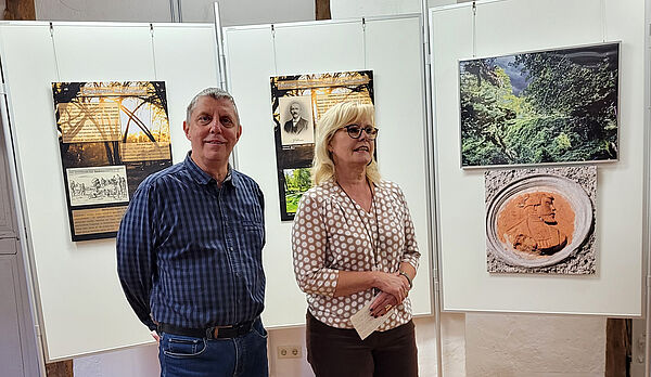 Ein Mann und eine Frau stehen vor drei Aufstellern. Auf den Aufstellern befinden sich Infotafeln und Bilder.