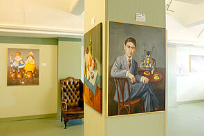 Blick in die Ausstellung. Drei Porträts hängen an der Wand. Ein Stuhl steht im Raum.