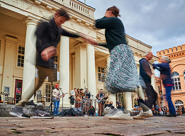 Auf einem Marktplatz spielen Musiker. Zuschauer tanzen.