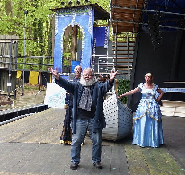 Wolfgang Bordel steht mit zwei Schauspielern auf der Bühne und hebt die Arme hoch.