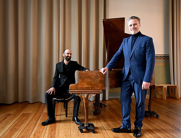 Zwei Musiker auf der Bühne. Einer steht. Einer sitzt am Klavier.