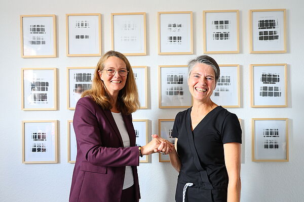 Zwei Frauen stehen vor Kunstwerken und reichen sich die Hände.