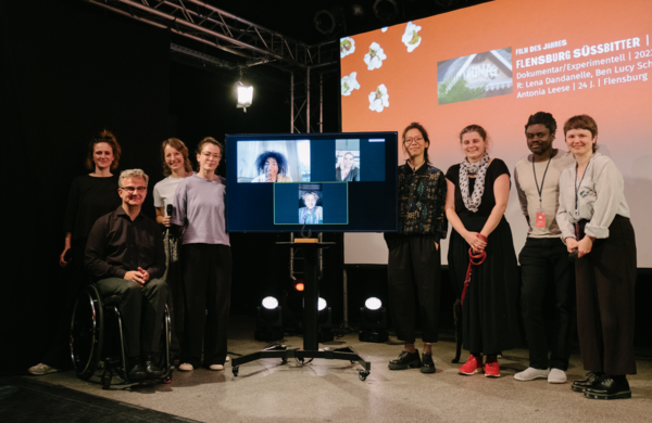 Acht Personen auf der Bühne, drei weitere sind auf dem Bildschirm zugeschaltet.