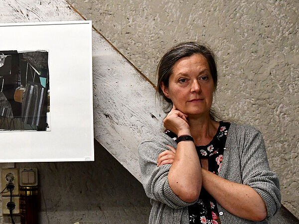 Ein Mann und eine Frau stehen in einem Atelier. Ein Bild hängt zwischen ihnen.