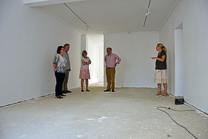 Zwei Männer und drei Frauen stehen ein einem leeren, weiß gestrichenen Raum und unterhalten sich.