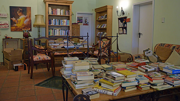 Ein Raum. Darin befinden sich Tische und Regale voller Bücher. Dazwischen stehen Sessel und Stühle.
