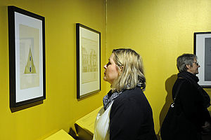 Eine Frau betrachtet Zeichnungen an einer gelben Wand.