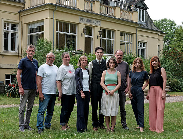 Eine Villa mit der Aufschrift "Pension Möwe". Davor stehen Darsteller, Produktionsteam und Unterstützer zum Gruppenfoto bereit.