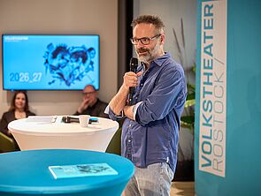 Ein Mann steht an einem Tisch und spricht ins Mikrofon.
