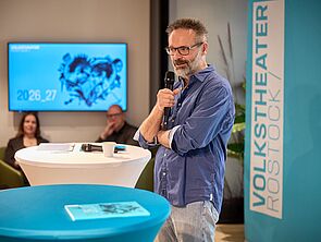 Ein Mann steht an einem Tisch und spricht ins Mikrofon.