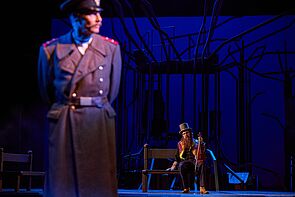 Ein Mann in Uniform wird beleuchtet. Im Hintergrund sitzt ein Mann.