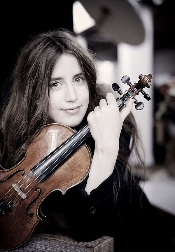Ein Porträt von Vilde Frang. Sie stützt ihr Kinn auf ihre Violine.