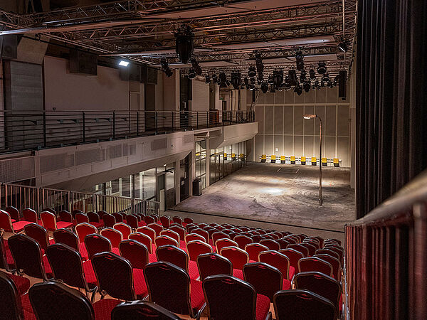 Ein Theaterraum. Er hat eine Bühne und viele rote Sitzreihen.