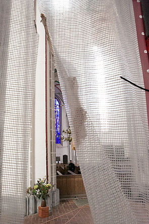 Blick durch einen leicht geöffneten Vorhang in die Kirche.