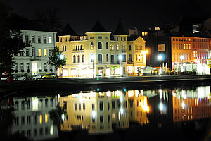 Der Schweriner Pfaffenteich bei Nacht. Straßenlichter erhellen die historischen Häuser am Südufer. Häuser und Licht spiegeln sich im Wasser.
