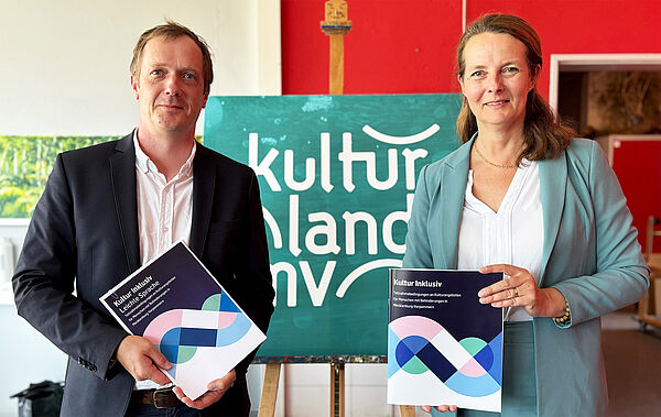 Ein Mann und eine Frau stehen nebeneinander. Jede Person hält ein Exemplar des Berichts in der Hand.