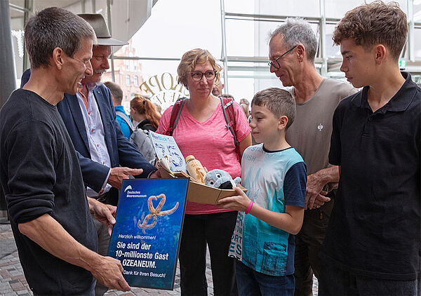 Die beiden Museumsdirektoren stehen vor einer vierköpfigen Familie. Sie überreichen ihr eine Urkunde und Geschenke.