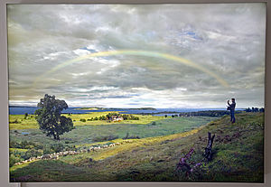 Ein Gemälde mit Wiesen, Hecken, einem Baum und einem Regenbogen am Horizont.