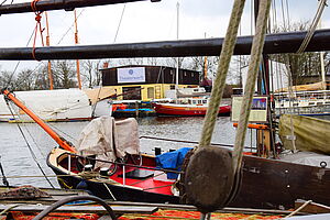 Am Ufer der Ryck ankern Segelboote. Dahinter, auf der anderen Uferseite, steht die Theaterwerft.