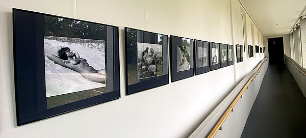 Ein langer Flur. An der Wand hängen Schwarz-Weiß-Fotos nebeneinander. 