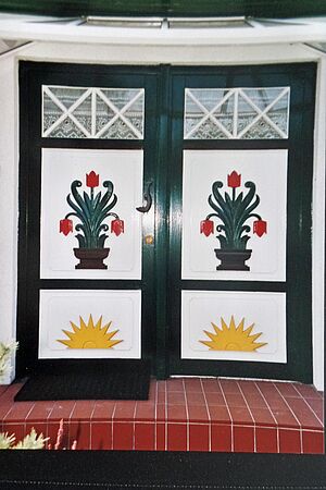 Eine Darßer Haustür in den Farben Weiß, Dunkelgrün, Gelb und Rot. Die Ornamente zeigen Blumen und eine aufgehende Sonne.