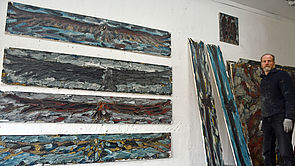 An einer Wand hängen vier balkenartige Leinwände untereinander. An der Wand lehnen noch zwei. Daneben steht der Künstler. 