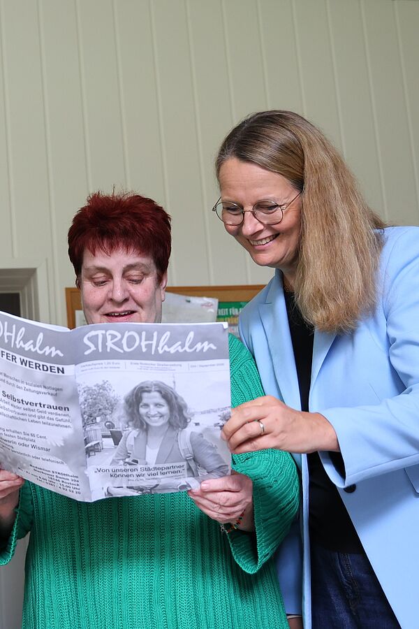 Zwei Frauen blicken in eine Zeitung.