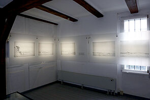 Beleuchtete Bilder hängen an der Ausstellungswand.