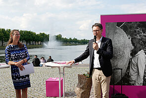 Zwei Personen im Gespräch. Sie stehen an einem Tisch am Rande des Wassers.