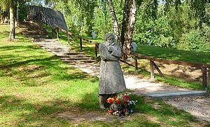 Auf einer Wiese steht eine Skulptur. Davor liegen Blumen.